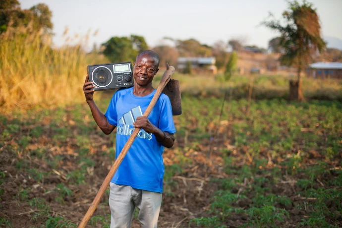 A man standing in a field holding a radio and a stick